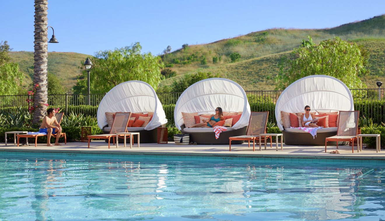 Exterior view of people lounge near pool at Los Olivos at Irvine Spectrum Apartment Homes in Irvine, CA.